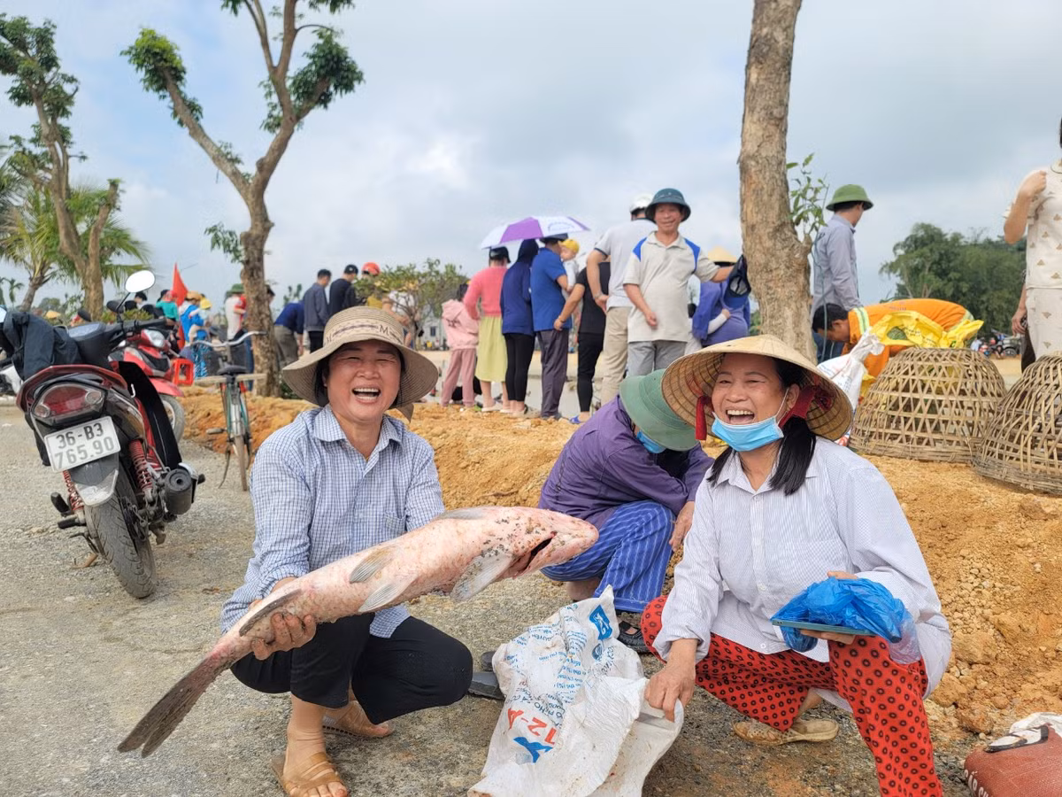 Những người phụ nữ đứng trên bờ vui vẻ đón cá của người thân bắt được.