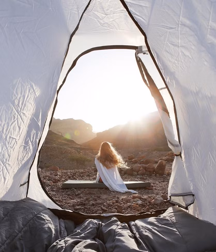Cô gái ngồi giữa cảnh đất đá, đón ánh nắng mặt trời được nhìn qua khung lều trắng tại vùng Wadi Araba, nằm gần quốc gia Jordan, Trung Đông. Ảnh: Roundtheworldgirl/Instagram.