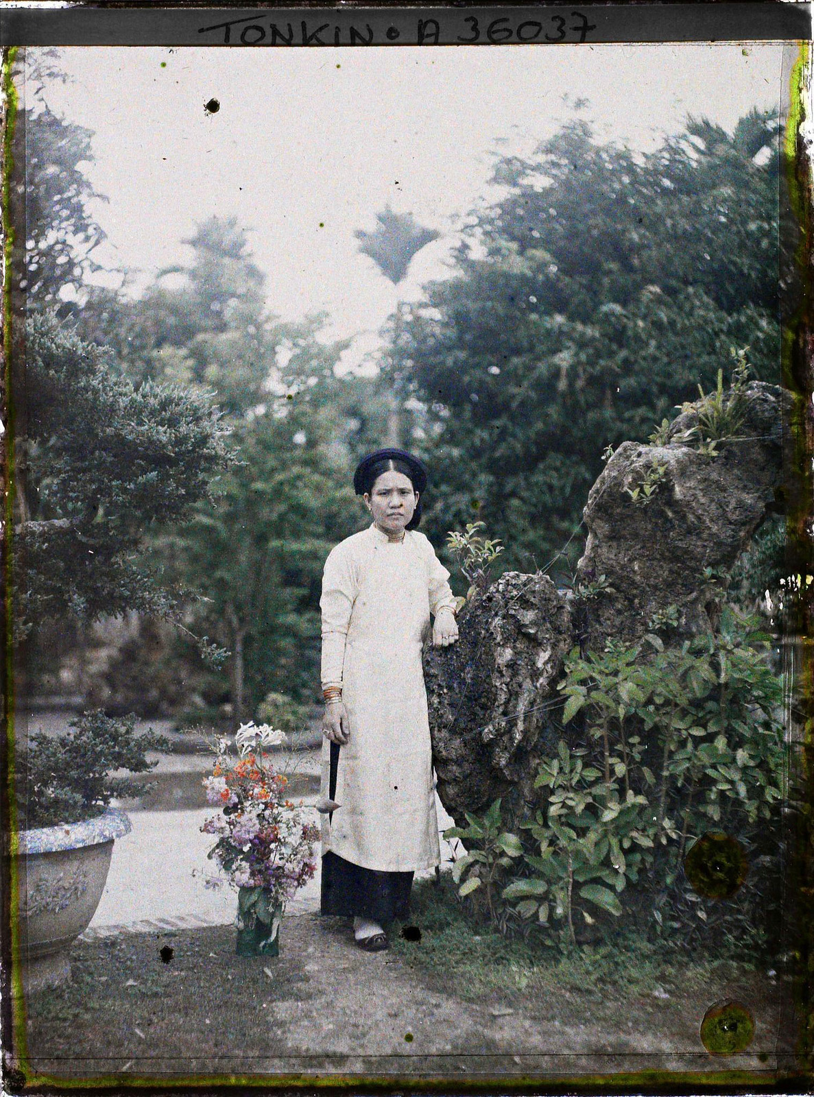 Cô gái đứng tựa vào hòn non bộ trong một khu vườn.