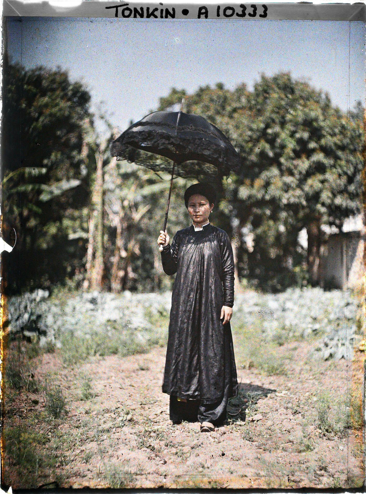 Người phụ nữ mặc áo dài đen, cầm chiếc ô kiểu châu Âu có viền ren đen.