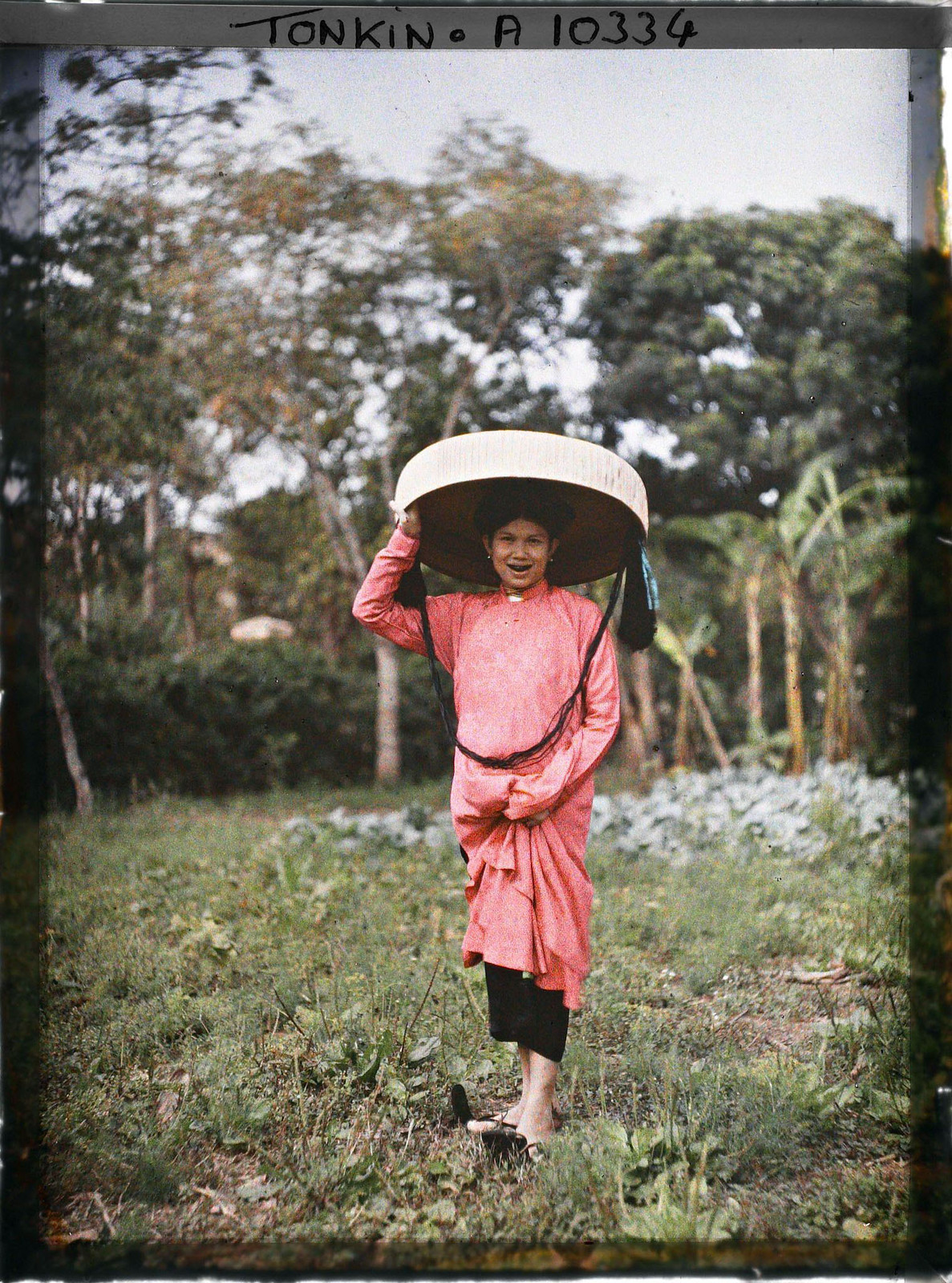 Người phụ nữ cười toe toét trong trang phục cự tiệc, với áo dài hồng và nón quai thao.