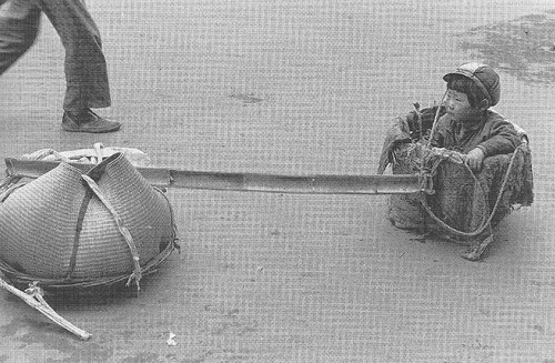 Em bé đi tị nạn ngồi một bên quang gánh.