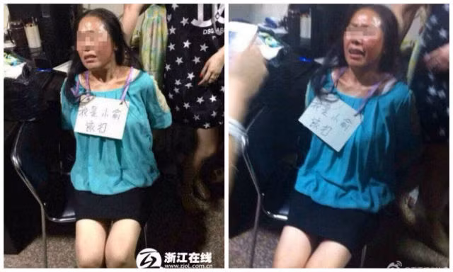 Chủ cửa hàng bắt kẻ trộm đeo tấm biển "Tôi là kẻ trộm. Tôi đáng bị đánh" lên cổ và xung quanh có nhiều người lấy điện thoại ra quay phim, chụp ảnh.