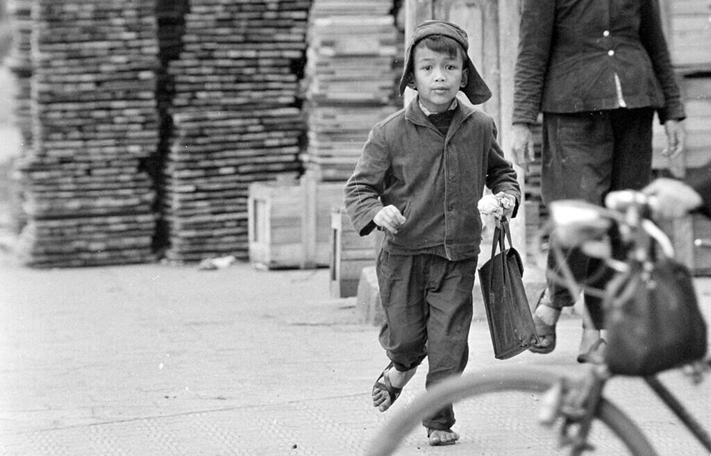 Một chú bé cầm bánh và cặp trên tay, vội vã chạy đến trường, 27/3/1973.