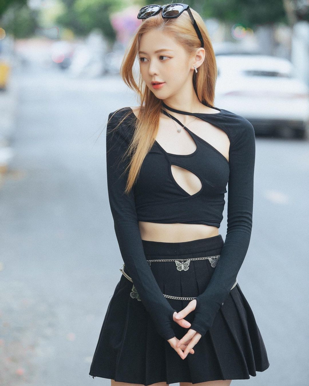 Kết hợp với áo, cô chọn mặc chân váy tennis cùng màu. Ngoài ra, cô còn đeo boots đùi bằng da và sử dụng kính mắt to bản. Tổng thể trang phục tuy không rực rỡ về màu sắc nhưng vẫn ấn tượng vì hình ảnh đa dạng nó mang đến cho người mặc. Đó là sự nữ tính vừa đủ đan xen nét năng động và cả quyến rũ.