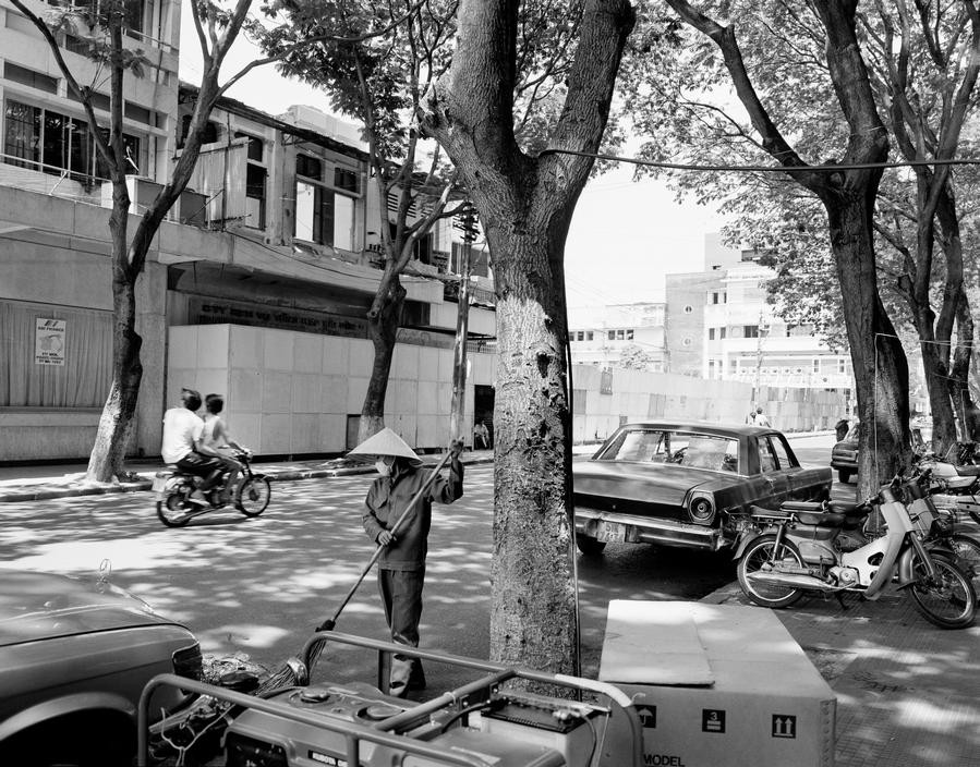 Một con đường ở TP HCM với những chiếc Honda Cub dựng trên vìa hè. Trên đường, hai nam giới đèo nhau trên xe Honda 67.