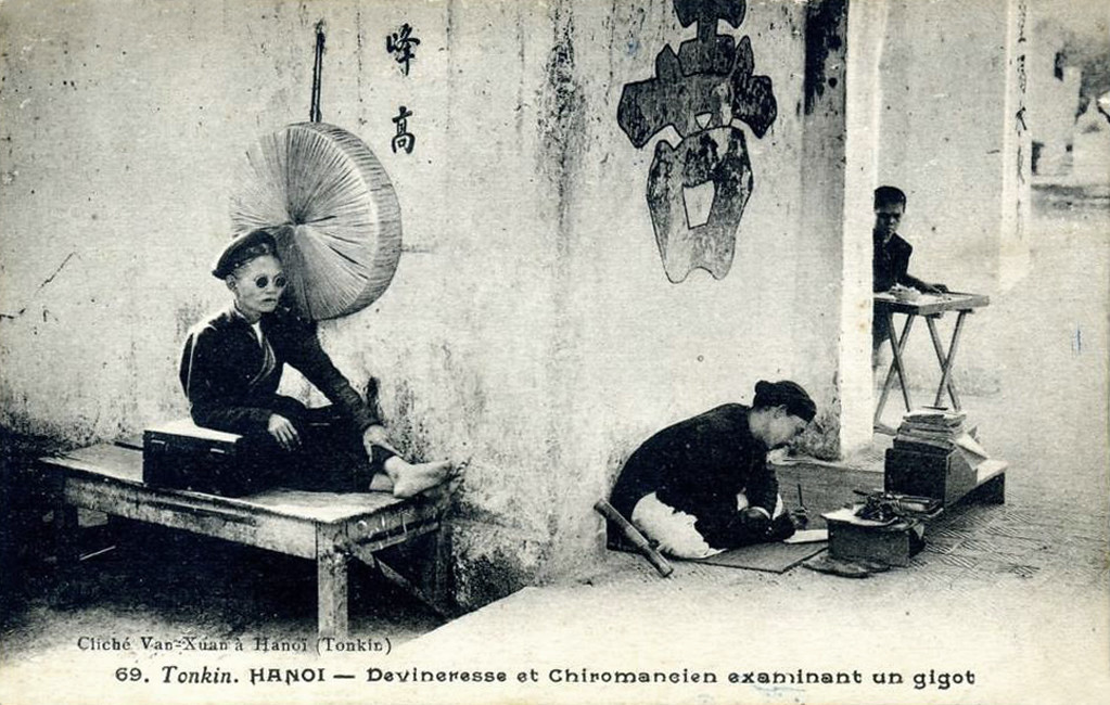 Bà thầy bói và thầy tướng số hành nghề bên ngoài một ngôi đền ở Hà Nội khoảng cuối thế kỷ 19, đầu thế kỷ 20.
