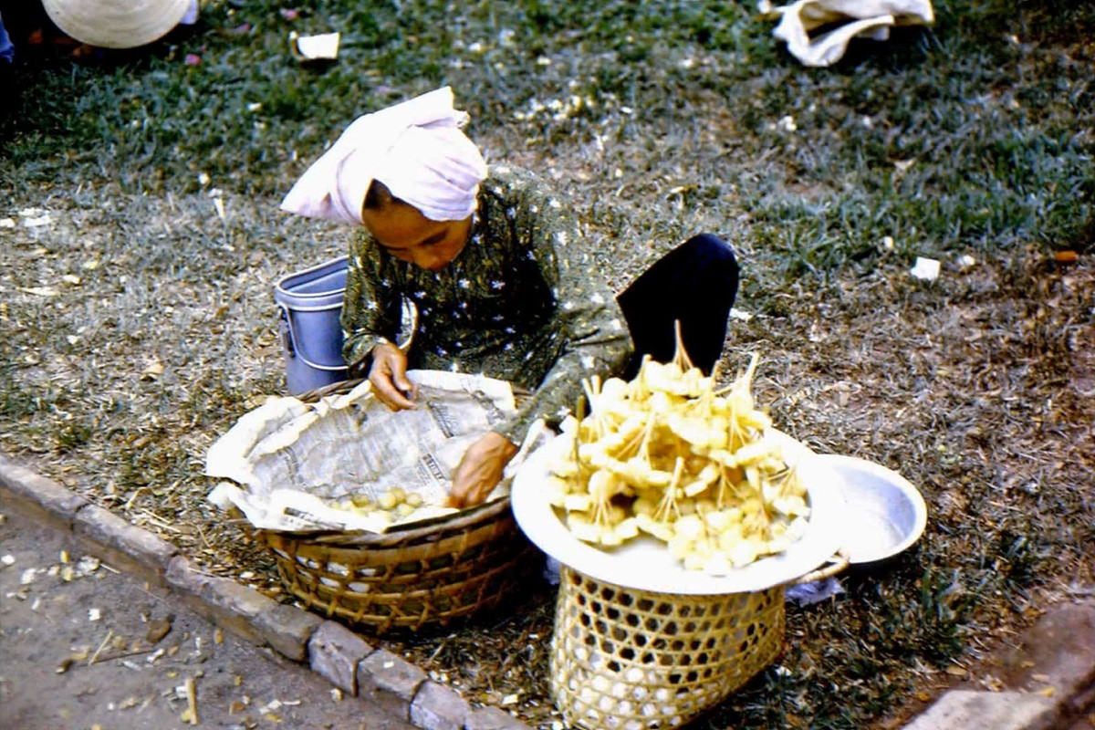 Quầy mía ghim của một cụ bà, 1964. Đây là một món ăn rất đơn giản, là thân mía tươi róc vỏ, cắt khúc vừa ăn rồi ghim vào que tre để cầm tay cho tiện. Ảnh: Donald Pickett.