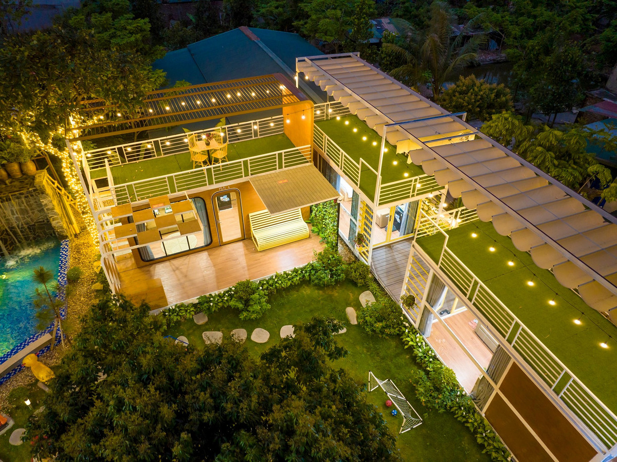 Khu nhà đẹp như mô hình DIY với bể bơi bao quanh nhà, điều hòa không khí mát mẻ. Khung cửa kính kết nối thiên nhiên. Sân vườn sắp đặt tiểu cảnh, xích đu, cầu trượt cho trẻ và bàn trà cho người lớn.