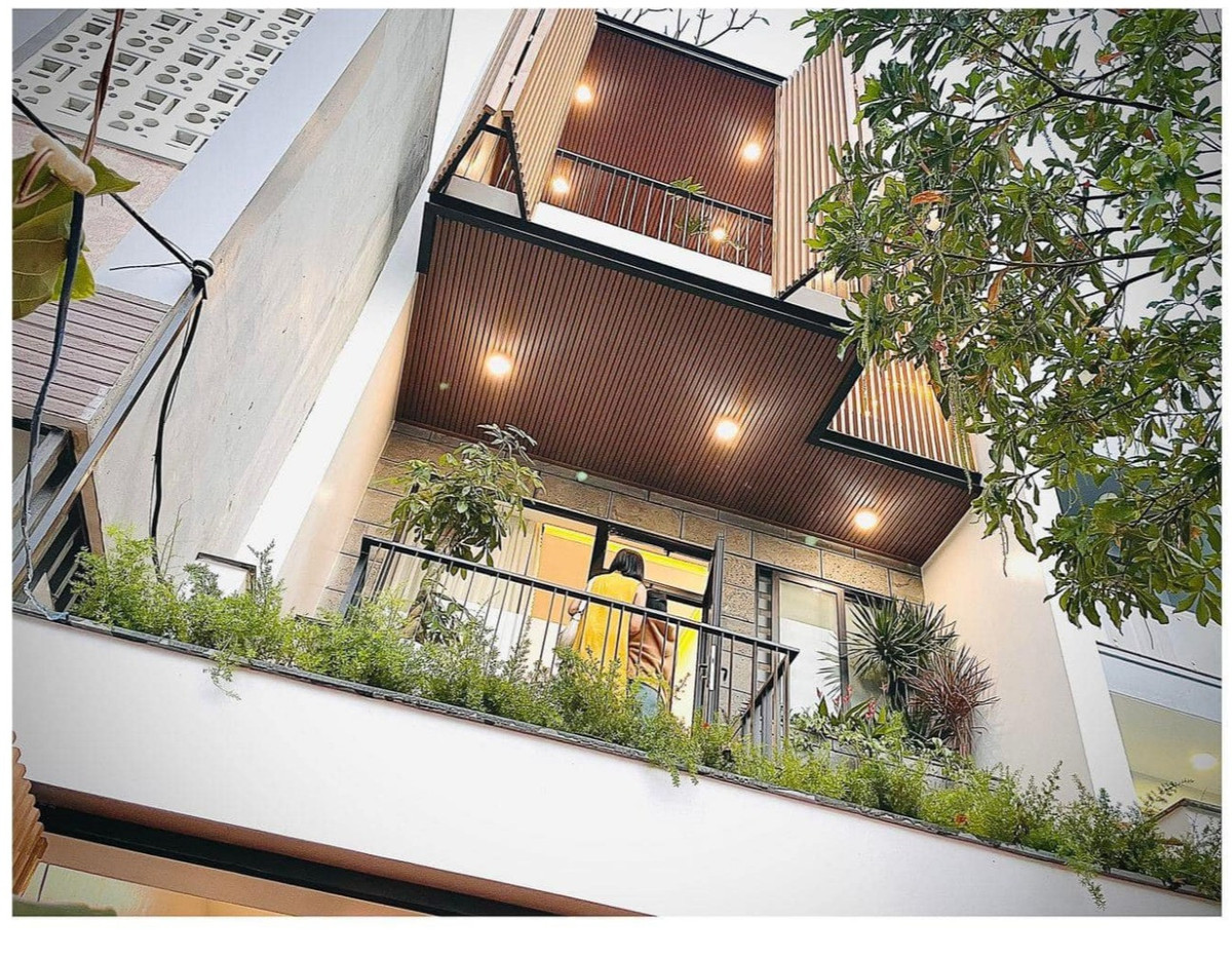 Ban công tầng 2 với hệ kính mở, phía trước là bồn trồng cây dạng cỏ. Trần hiên ban công ốp gỗ nhựa.