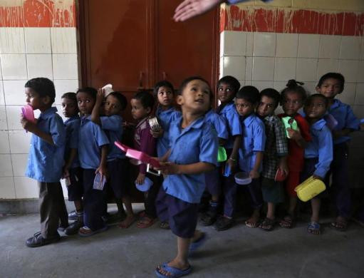 Các em học sinh tại New Delhi cầm hộp cơm xếp hàng chờ lấy cơm trưa miễn phí.