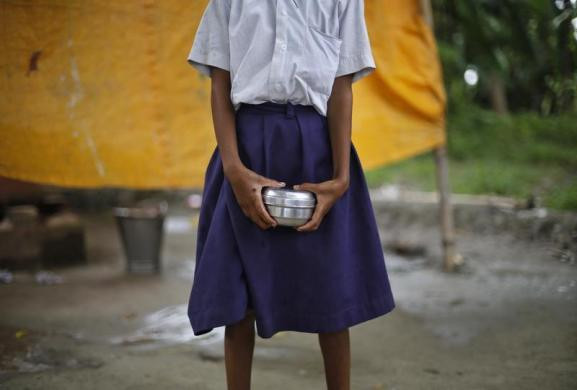 Một bé gái cầm chiếc hộp inox đựng cơm chờ nhận được bữa trưa miễn phí tại trường học.