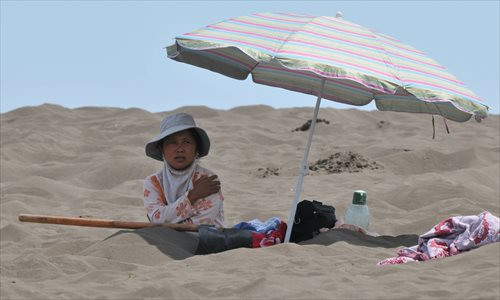 Một phụ nữ ở Turpan, khu vực tự trị Tân Cương chôn chân trong cát nóng. Họ cho rằng liệu pháp này có thể chữa một số bệnh mãn tính, bao gồm viêm khớp dạng thấp và huyết áp cao.