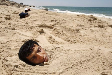 Các bệnh nhân tại Khan Younis, Palestinin vùi thân mình trong lớp cát trên bãi biển để chữa bệnh ngoài da và cơ.