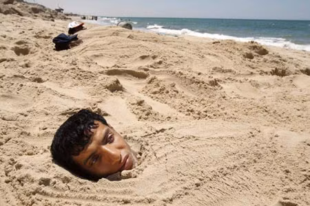 Các bệnh nhân tại Khan Younis, Palestinin vùi thân mình trong lớp cát trên bãi biển để chữa bệnh ngoài da và cơ.