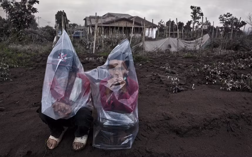 Hai em nhỏ trùm kín người bằng túi ni lông tránh tro bụi núi lửa.