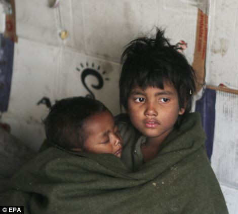 Một cậu bé sống ở khu ổ chuột thành phố Srinagar trùm chiếc mền mỏng ôm chặt đứa em nhỏ đang ngủ say.