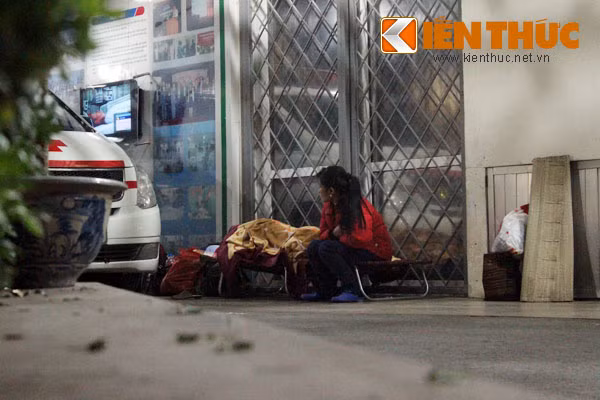Một phụ nữ ngồi so vai trong gió lạnh, chờ người thân đi cùng đang đến "ca" ngủ.