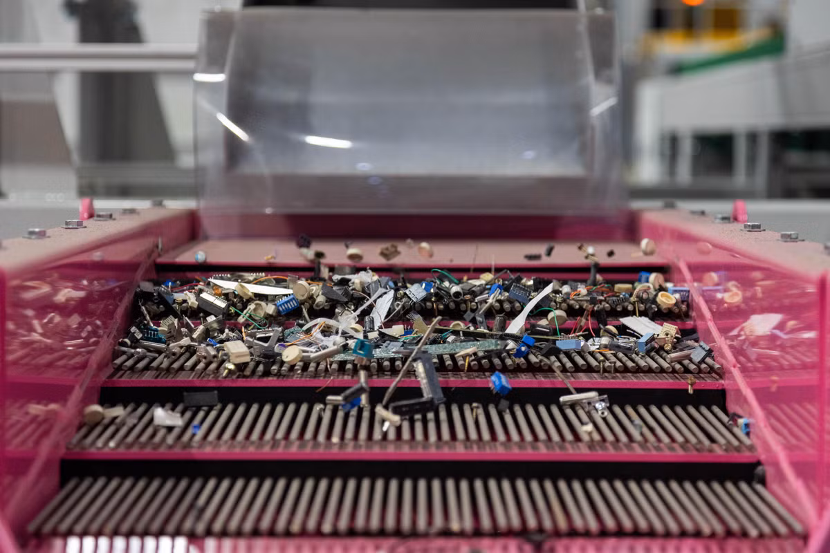 Sau đó, bảng mạch và các linh kiện như vi mạch, tụ nhôm được chuyển sang một máy phân loại lớn màu hồng. Các mảnh linh kiện di chuyển trên băng chuyền rung giống như rây lọc, rơi vào các thùng khác nhau tùy theo kích thước.