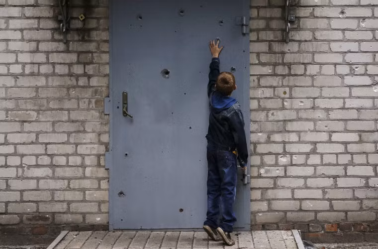 Một cậu bé đang cố cho tay vào lỗ đạn trên cửa nhà.