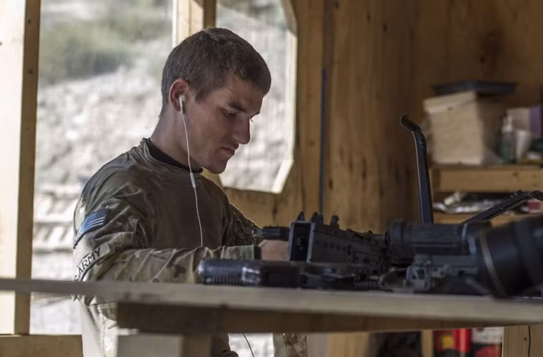 Một binh sĩ Mỹ đang làm sạch băng đạn súng máy trong khi nghe nhạc từ iPod.