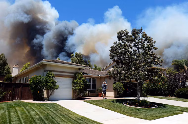 Một người đàn ông gọi điện thoại khi ngọn lửa cháy rừng tiếp cận ngôi nhà của người hàng xóm tại thành phố Carlsbad, tiểu bang California.