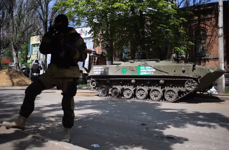 Một phần tử vũ trang đứng gác bên xe bọc thép BTR-D ở thành phố Slavyansk. Ngày 16/4, đã có 6 xe bọc thép của Quân đội Ukraine cùng kíp lái chuyển sang ủng hộ người biểu tình.