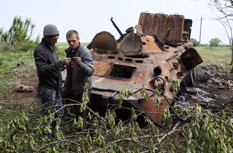 Người dân địa phương bên cạnh một chiếc xe bọc thép bị đốt cháy sau cuộc đụng độ giữa lực lượng Tự vệ Donetsk và quân đội Ukraine ở gần Kramatorsk.