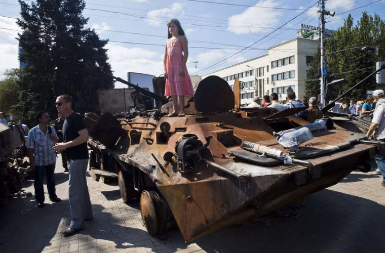 Một bé gái chụp ảnh với xe chiến đấu bộ binh của Quân đội Ukraine bị lực lượng ly khai phá hủy.