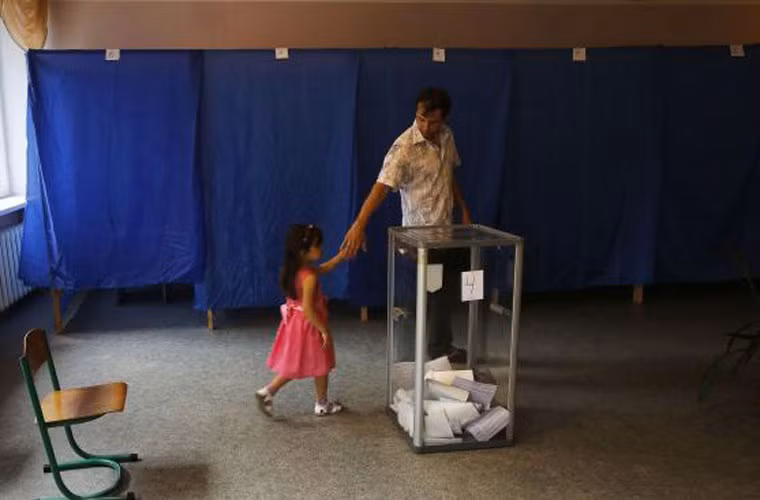 Người đàn ông dẫn con gái đi bỏ phiếu bầu cử tổng thống Ukraine tại điểm bỏ phiếu thị xã Krasnoermeisk, phía tây tỉnh Donetsk.