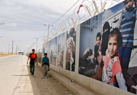 Trẻ em tị nạn người Syria đi gần bức tường của trụ sở chính Ủy ban Người tị nạn Liên Hiệp Quốc gần thành phố Mafraq, Jordan vào ngày 24/3/2014. Khoảng 8 triệu người Syria đã phải bỏ nhà sau khi cuộc nội chiến nổ ra vào tháng 3/2011.