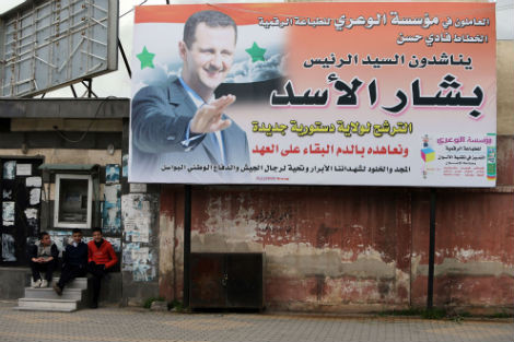 Những người thanh niên Syria ngồi cạnh tấm poster có chân dung Tổng thống Bashar al-Assad ở thành phố phía tây Syria Homs vào ngày 13/3/2014.