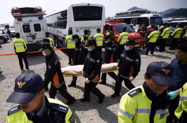 Đội cứu hộ chuyển thi thể của hành khách xấu số vừa được tìm thấy trong phà Sewol lên đảo Jindo giữa 2 hàng cảnh sát. Thợ lặn đã tìm thấy 16 thi thể trong phà Sewol nâng tổng số người thiệt mạng lên 58 người.