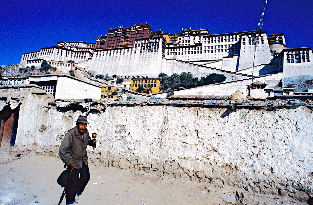 Người đàn ông cầm bánh xe cầu nguyện đi qua khu vực cung điện Potala.