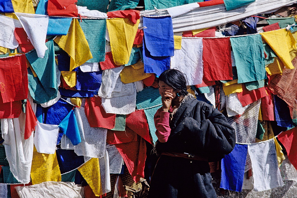 Người phụ nữ Lhasa đi qua những lá cờ lung ta, loại cờ cầu nguyện của với Phật giáo Mật tông Tây Tạng.