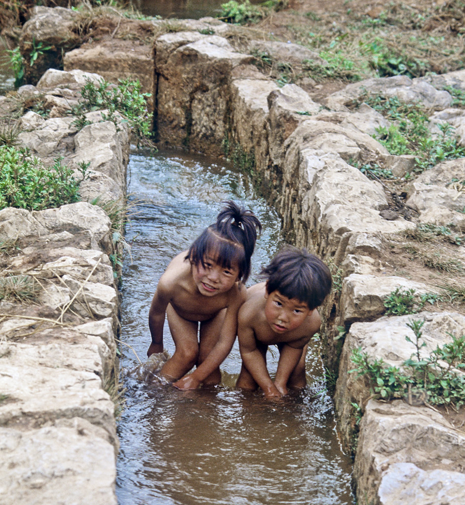 Hai em bé nghịch nước dưới mương thủy lợi.
