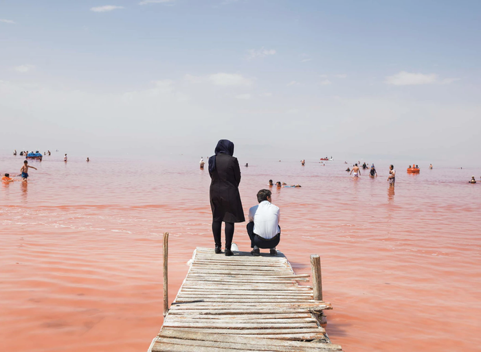 Ảnh chụp tại Iran, 2016. Người dân đang tắm tại một vùng nước thuộc hồ Urmia. Khu vực này có màu đỏ hồng do có chứa các loài tảo và vi khuẩn nước mặn. Người Iran từ nhiều thế hệ thường tới du lịch tới đây, nhưng lượng khách ngày càng giảm khi diện tích hồ dần bị thu hẹp lại vào những năm 1980. Gần đây, mực nước hồ đã dần hồi phục, nhưng vẫn chỉ bằng một nửa so với kích thước ban đầu.