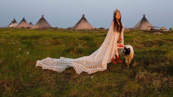 Ảnh chụp tại Nga, 2016. Khoác một tấm màn và đội vương miện bằng bìa cứng, cô bé Kristina Khudi hóa thân thành "công chúa lãnh nguyên" trong khu cắm trại Nenets gần vùng biển Kara. Suốt nhiều thế kỷ, những người chăn nuôi tuần lộc ở Bắc Cực, Nga lại di cư 800 dặm mỗi năm. Nhưng giờ đây, hành trình của họ đối mặt với nhiều trở ngại, ngoài thách thức đến từ tự nhiên là các vùng khí đốt khổng lồ, còn là thách thức của thế giới hiện đại: biến đổi khí hậu.