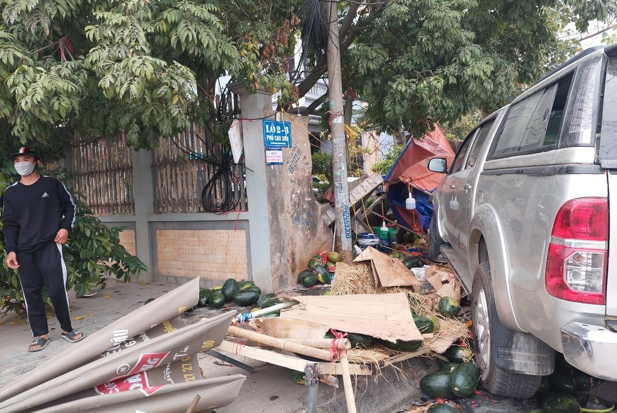 Do mất lái, xe ô tô biển xanh tiếp tục lao vào quán bán hoa quả ven đường, lúc này có 2 người đang ngồi bán hàng.