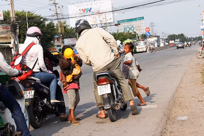 Chúng tôi theo chân nhóm khoảng 18 người, hơn 2/3 là các em nhỏ thường tụ tập ăn xin ở ngã ba Long Cang, gần cầu Bến Lức (H.Bến Lức, Long An). Từ sáng sớm các em nhỏ này xuất hiện rồi chớp nhoáng chia nhau rẽ đi các khu vực, các trụ giao thông đông người qua lại để xin tiền. Mỗi nhóm có chừng 3 - 8 thành viên lớn nhỏ, đứa lớn trên 10 tuổi, đứa bé nhất chưa đầy 2 tuổi. Trong ảnh: Khi đèn đỏ, đứa chặn đầu, đứa ngửa tay xin buộc người đi đường phải móc tiền ra cho.