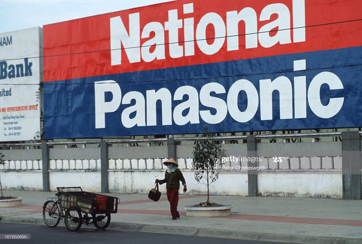 Người phụ nữ và chiếc xe ba gác phía dưới pa-no ngoại cỡ của hãng National, Panasonic trên đường phố Sài Gòn.