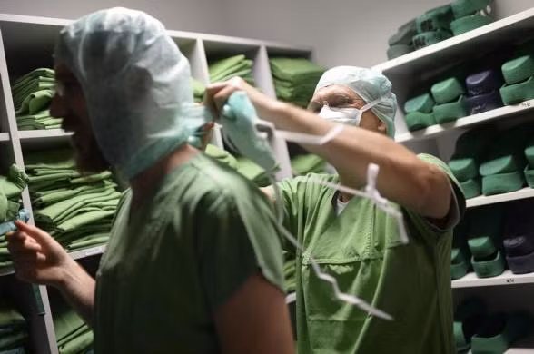 Giáo sư Karl Oldhafer đang được một thành viên trong nhóm phẫu thuật chuẩn bị trang phục trước khi vào phòng phẫu thuật.