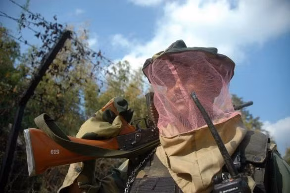 Nhân viên an ninh Ấn Độ đeo mặt nạ chống muỗi được phát bởi đơn vị y tế mỗi khi đi tuần.