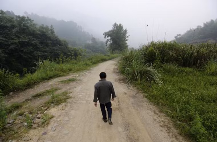 Ông Xiong Dejun đi bộ trên con đường làng đến bệnh viện làng Heshan để chụp X – quang phổi.