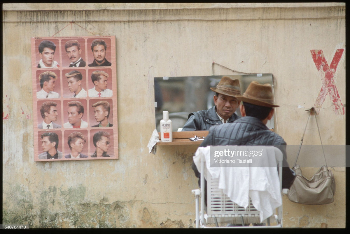 Người thợ cắt tóc chợ đợi khách hàng tại hiệu cắt tóc đường phố của mình.
