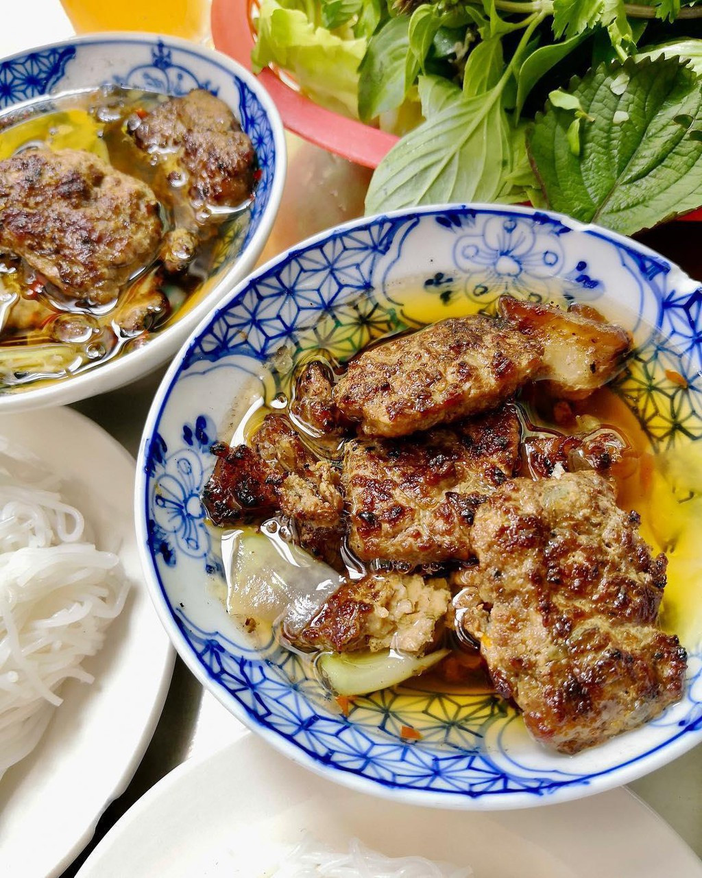  Bún chả Hà Nội có 2 loại chả chính: chả viên thường được làm từ thịt nạc lợn băm nhuyễn, ướp gia vị, vo viên, ấn cho hơi dẹp và nướng; còn chả miếng thường dùng thịt nách hoặc thịt ba chỉ, thái mỏng, cũng ướp gia vị tương tự chả viên và đem nướng vàng. Ăn kèm bún chả còn có thêm nem rán, nem cua bể, nước mắm pha loãng, có đu đủ xanh, su hào, cà rốt, các loại rau thơm... Ảnh: Thon.foodie.