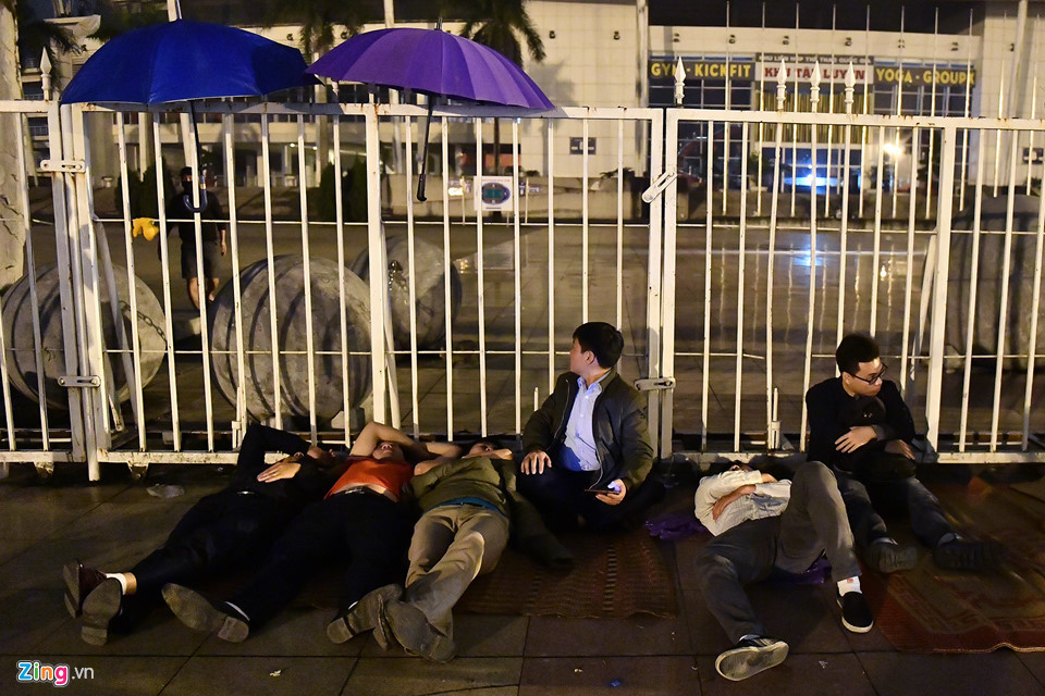 Một nhóm thanh niên dùng ô gác lên hàng rào che những hạt mưa bụi bắt đầu trút xuống.