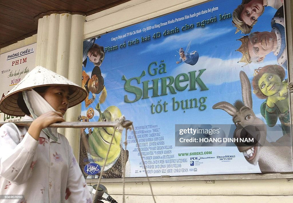 Người bán hàng rong đi ngang qua rạp Tháng Tám trên phố Hàng Bài, nơi đang chiếu bộ phim hoạt hình Mỹ Shrek II, 18/8/2004.