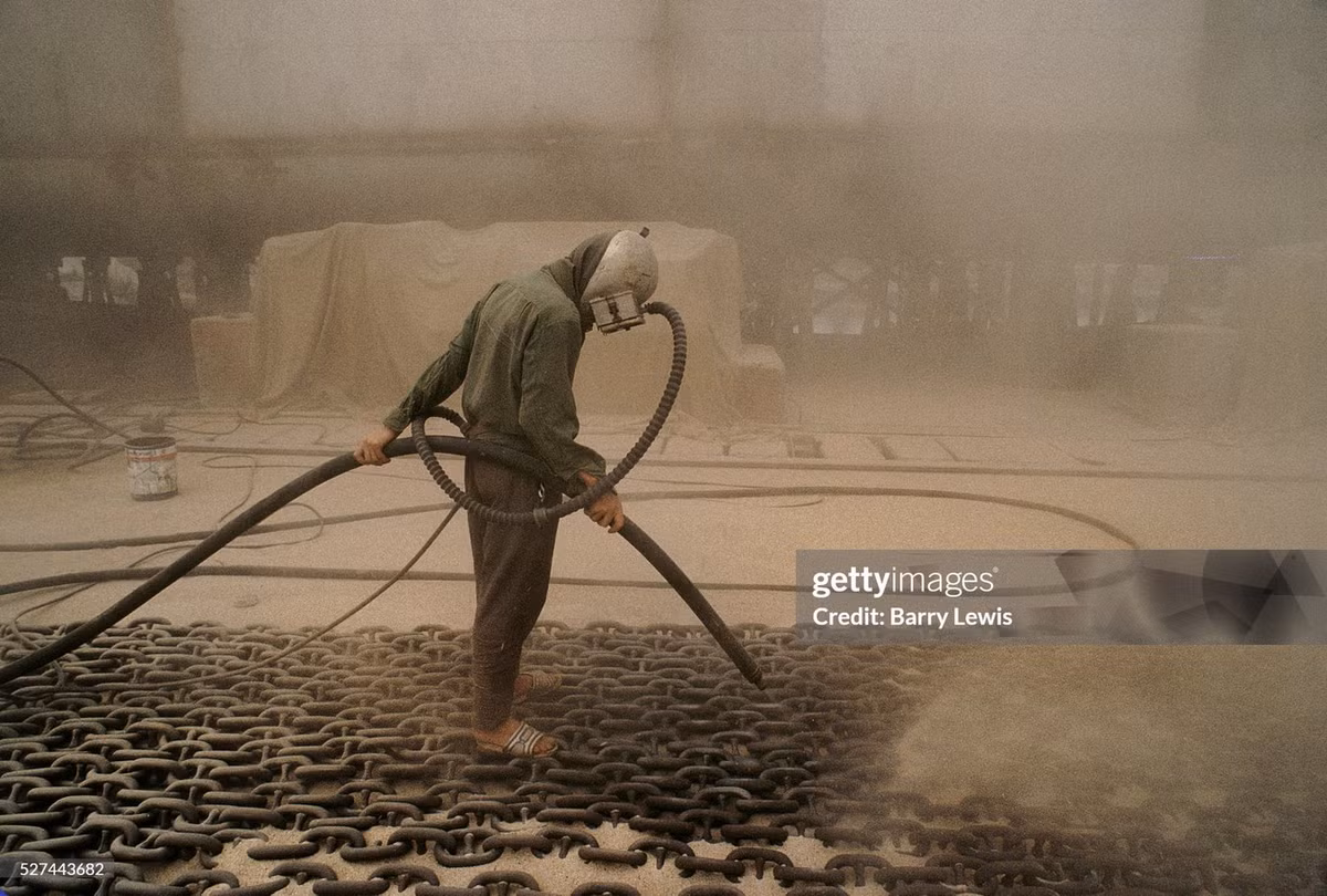 Người công nhân đeo mặt nạ bảo hộ làm sạch dây xích neo tàu bằng máy phun cát tại bãi vận chuyển.