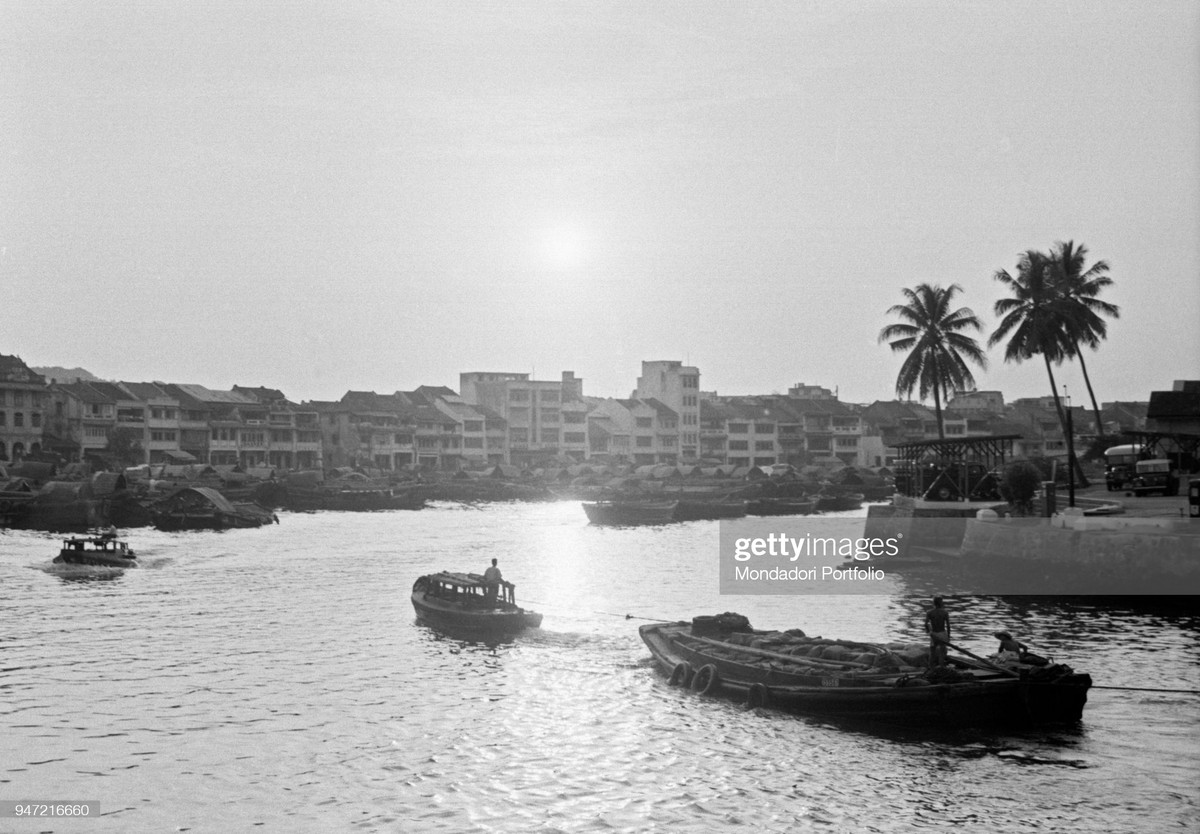 Những con thuyền di chuyển trong ráng chiều trên sông Singapore, 1962. Bên bờ sông là khu phố thương mại sầm uất với những ngôi nhà san sát.